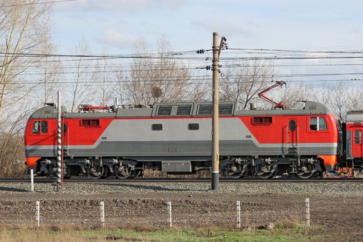 Red locomotive on electricity coming by rail.