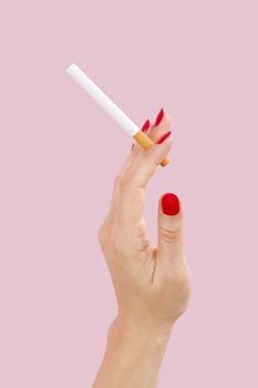 Female hand holding cigarette isolated on pink background. Feminine tobacco abuse.