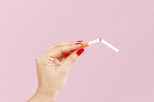Last cigarette. Female hands with red fingernails breaking the last cigarette isolated on pink background. Quit smoking new year resolution.