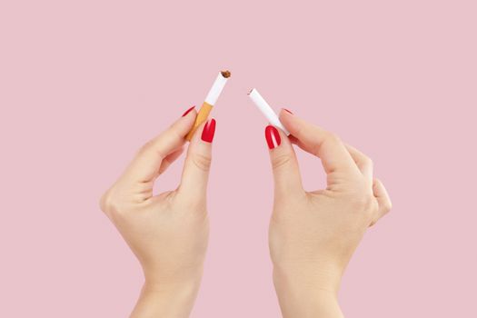 Last cigarette. Female hands with red fingernails breaking the last cigarette isolated on pink background. Quit smoking new year resolution.