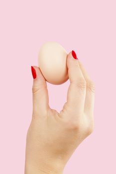 Female hand with red fingernails holding two eggs isolated on pink background. Feminism, emancipation, provocation and relationship problems.