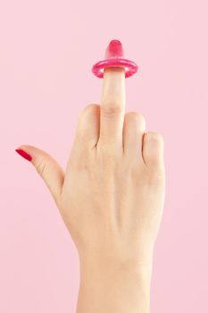 Female hand with red nails holding pink condom isolated on pink background. Safe sex and birth control concept. 