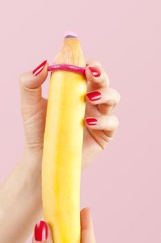 Female hand with red fingernails puts on a condom onto a banana. Safe sex concept.