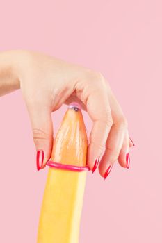 Female hand with red fingernails puts on a condom onto a banana. Safe sex concept.