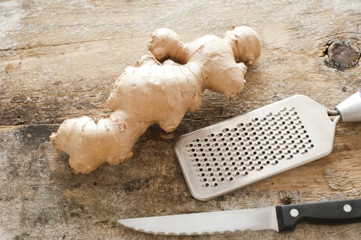 Section of whole raw root ginger on a rustic table with a stainless steel, grater and knife ready to be prepared as a healthy spicy ingredient for cooking