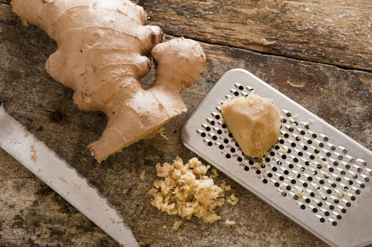 Freshly minced or grated root ginger on an old wooden kitchen table with a portion of whole root and a stainless steel grater or rasp