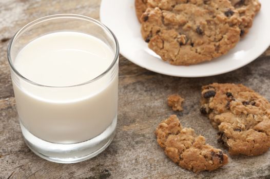 High Angle Close Up Still Life of Glass of Cold Refreshing Milk Beside Plate of Fresh Baked Cookies with Single Broken and Half Eaten Biscuit in Foreground
