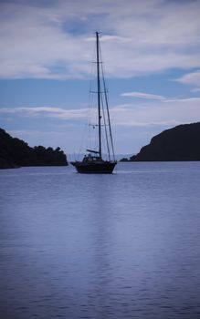 Yacht, mooring in a calm sea or ocean bay water in early blue lit morning.