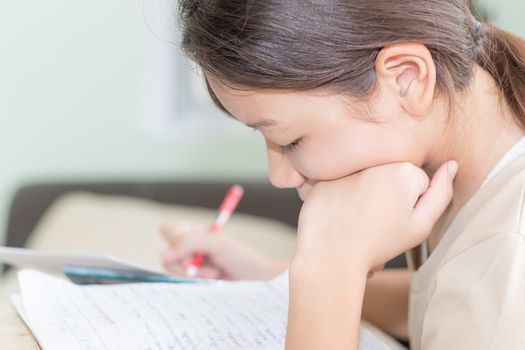 Asian girl doing her homework, writing on a lesson book