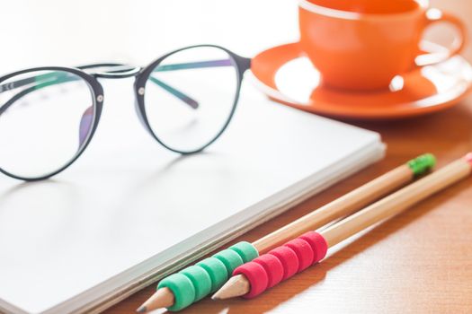 Pencils and eyeglasses on open blank white notebook with coffee cup on the desk, stock photo