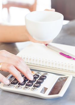 Woman's hands holding coffee cup and press calculator, stock photo