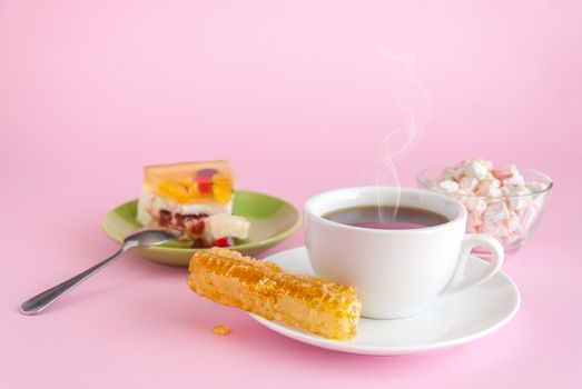 Cup of hot tea, honeycomb and cake on pink background