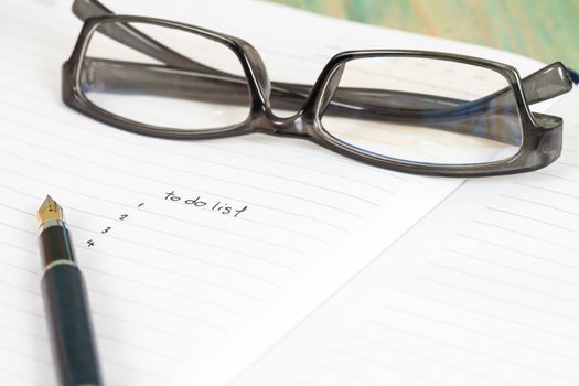 writing to do list on notebook page with pen on wood background