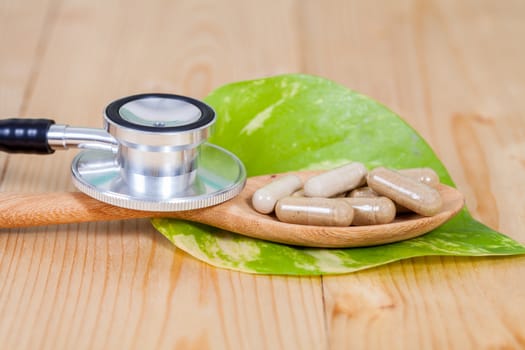 Capsules of herbs on spoon and stethoscope
