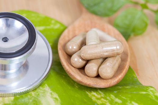 Capsules of herbs on spoon and stethoscope
