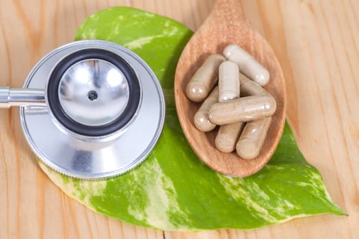 Capsules of herbs on spoon and stethoscope
