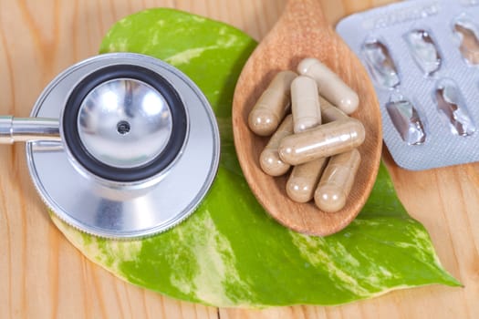 Capsules of herbs on spoon and stethoscope