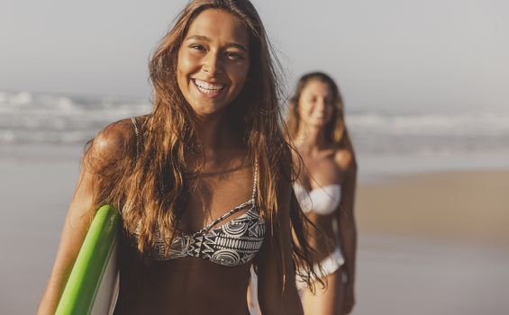 Best friends enjoying the summer, walking on the beach with a surfboard