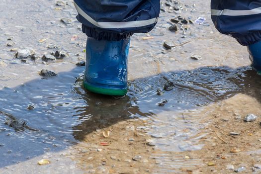 Child with blue rubber boots in a puddle. close up view