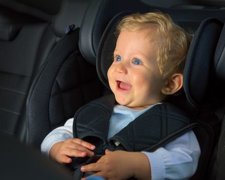 Baby boy 8 months old smiling in a safety car seat.