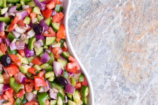 Colorful fresh Turkish shepherd salad served in a modern wavy dish over a stone background with copy space to the right in a close up overhead view