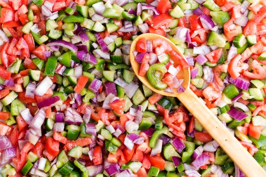 Colorful Turkish shepherd salad background food texture made from a variety of fresh finely diced vegetables with a wooden serving spoon viewed close up full frame from above