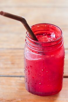 Iced drink in red glass on wooden table with vintage filter, stock photo