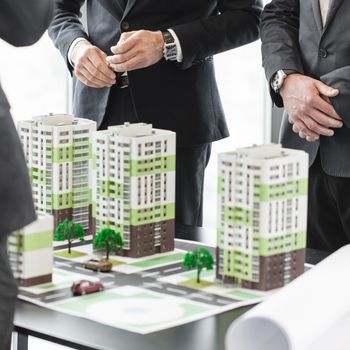 Business meeting of architects and investors looking at model of residential quarter houses