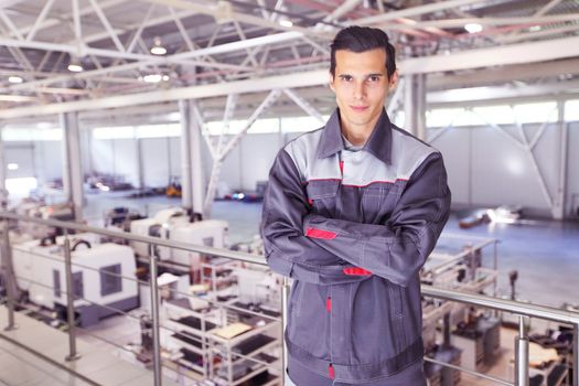 Young worker in uniform standing in CNC factory