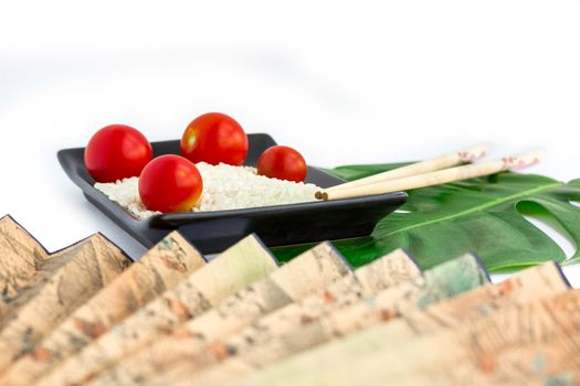 Oriental composition of rice, tomatoes, chopsticks, green leaf and transp isolated on white background