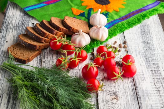 Still life on wooden background: tomatoes, black bread, garlic, fennel, bayberry pepper