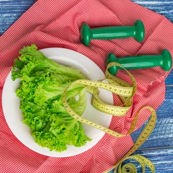 Fitness composition of green lettuce on white plate, weights and ruler