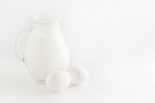 jug with milk and two eggs on white background.