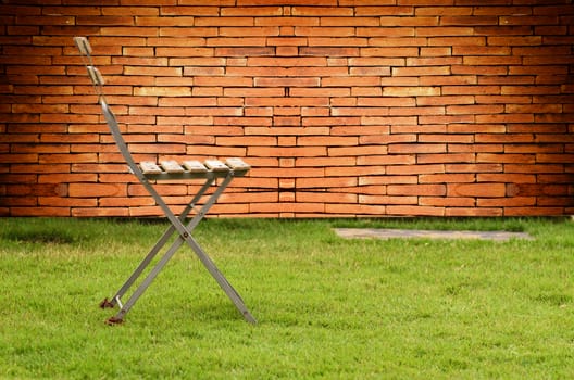 Old chair on green grass in brick wall background
