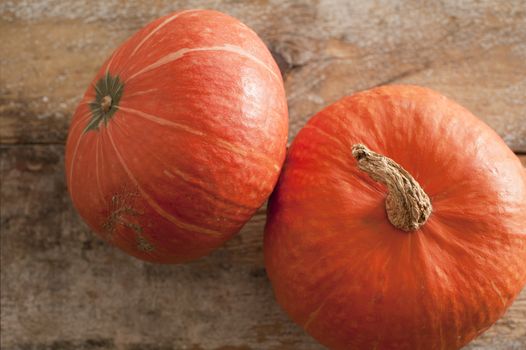 Two whole fresh orange pumpkins or seasonal squash viewed close up high angle on a wooden table