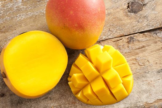 Fresh ripe tropical mango whole and sliced through to show the juicy flesh with a one section cut into a decorative hedgehog pattern , overhead on rustic wood