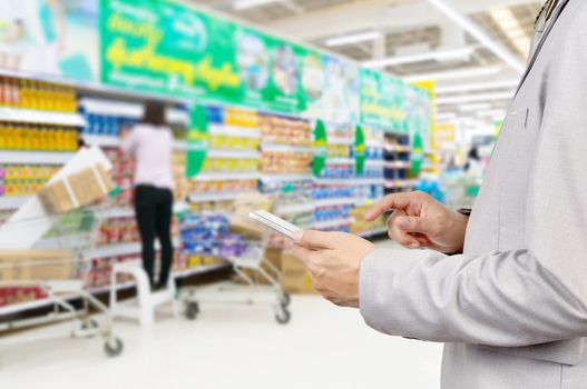 Hand of Businessman, Manger use Mobile Tablet in supermarket with Blur Background of Staff arrange product display on shelves in Supermarket or Hypermarket