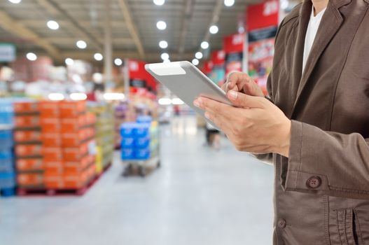 Hand of Businessman, Manger use Mobile Tablet in supermarket with Blur Background of product display on shelves in Supermarket or Hypermarket warehouse