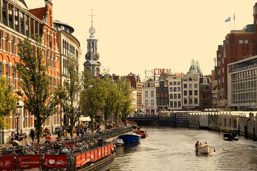 AMSTERDAM, THE NETHERLANDS - AUGUST 19, 2015: View on Bloemenmarkt and The Munttoren ("Coin Tower") from Koningsplein. People walk on the street Singel. Street life, Canal, bicycle and boat in Amsterdam. Amsterdam is capital of the Netherlands on August 19, 2015.