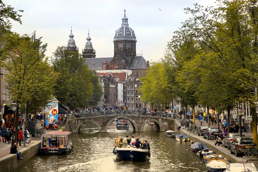 AMSTERDAM, THE NETHERLANDS - AUGUST 18, 2015: View on Saint Nicholas church or St Nicolaas kerk tower from Oudekennissteeg bridge. Street life, Canal, tourists and boat in Amsterdam. Amsterdam is capital of the Netherlands on August 18, 2015.
