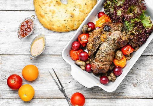 Meat knuckle of beef in the baking dish with tomatoes and plum sauce