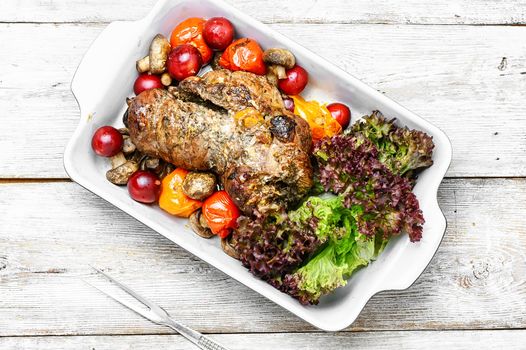 Meat knuckle of beef in the baking dish with tomatoes and plum sauce