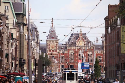 AMSTERDAM, THE NETHERLANDS - AUGUST 19, 2015: View on Amsterdam Central Station from Damrak street with row of shops; tram, tourists and bicycle iin Amsterdam. Amsterdam is capital of the Netherlands on August 19, 2015.