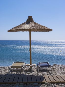 Reed umbrella and two deck chairs on the sea beach