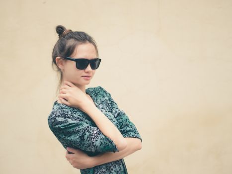 Fashionable serious young woman in black sunglasses posing near wall with copy space