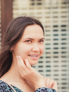 Close up of smiling young woman looking away and holding hand at face. Vertical portraite city outdoors