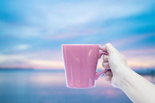 Woman hand holding coffee cup with sunset blur background 