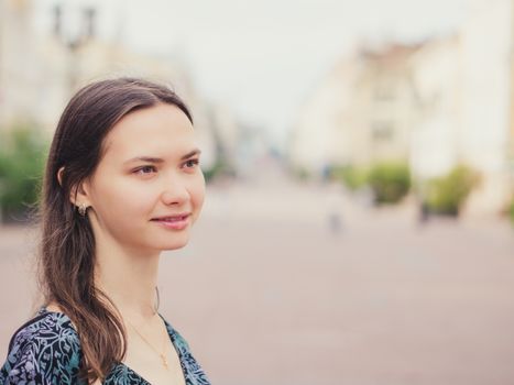 Close up of smiling young woman looking away. City outdoors with copy space