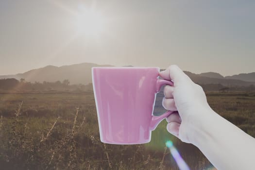 Woman hand holding coffee cup with sunrise, stock photo