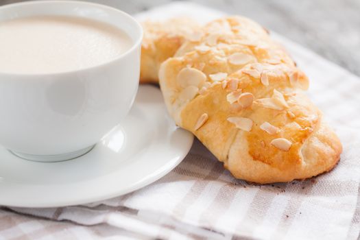 Two croissant with almonds and cup of cappuccino.